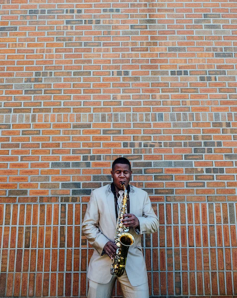  a man playing the saxaphone infront of a brickwall